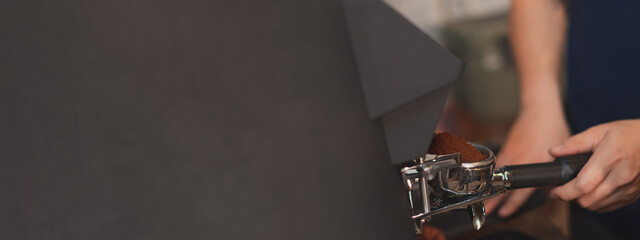 Close up of a hand holding a filter holder with ground coffee with loft gray copyspace background. Concept of modern warm coffee shop and Preparing process of coffee Banner, widescreen.