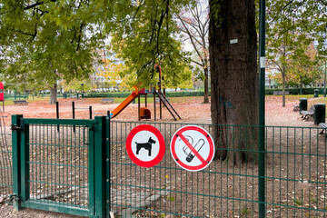 no smoking sign and no dogs allowed sign hanging on the fence of a public park in Brussels