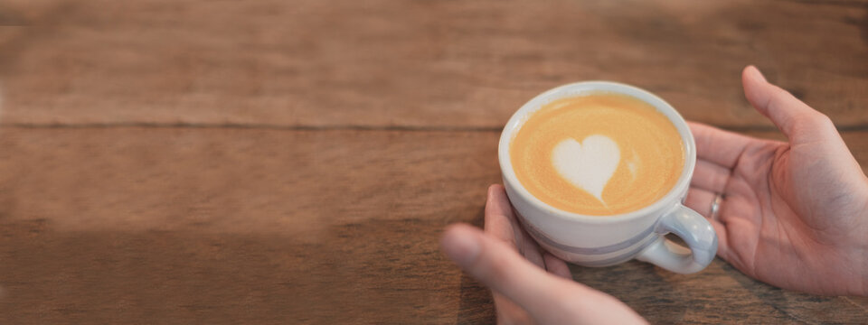 Vintage Tone Of Close Up Hand Holding Latte Art Coffee In Cappuccino Or Latte Cup At Cafe Or Coffe Shop. Concept Of Coffee Shop Banner Background With Copyspace. Widescreen And Panorama.