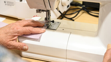 A woman sews a cloth with a sewing machine. The woman works in a factory. 