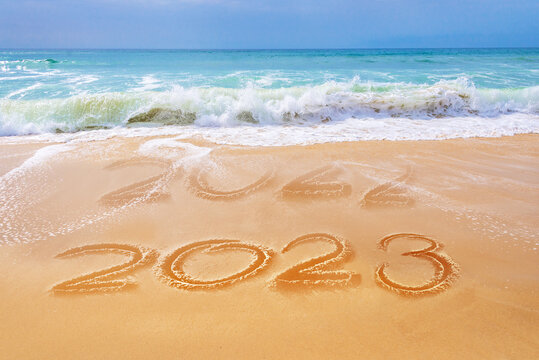 2023 written on the sand of a beach, ocean waves, travel new year greeting card