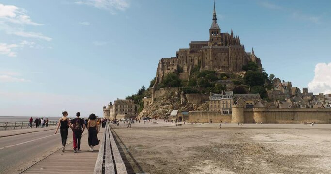 Several Tourists Walking On The Footbridge In Le Mont Saint-Michel In Normandy, France. Wide Shot
