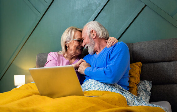 Smiling senior couple lying in bed in the bedroom using laptop.
