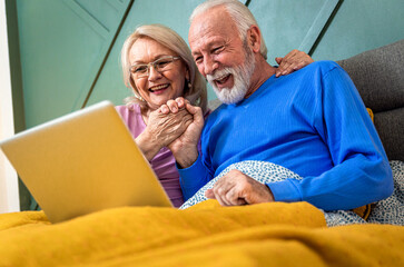 Smiling senior couple lying in bed in the bedroom using laptop.