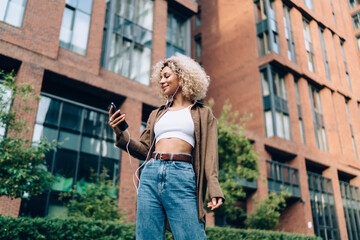 Ethnic woman in earphones browsing smartphone on street