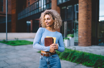 Content woman with books standing near building