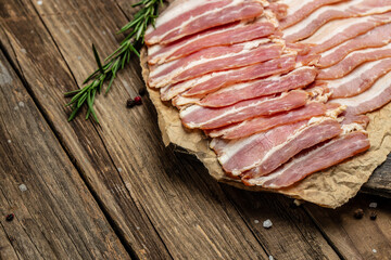 Raw smoked bacon slices with rosemary on wooden board. banner, menu, recipe place for text, top view