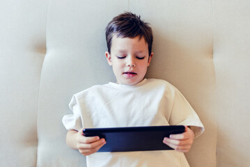Portrait of a happy boy watching videos online on a digital tablet at home and smiling - lifestyle concepts. Happy boy watching videos online on a digital tablet at home.