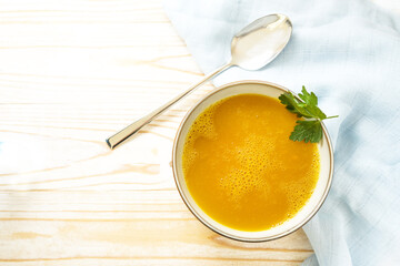 Carrot soup in a bowl on a light wooden table, healthy vegetable meal, recipe by professor Ernst Moro against diarrhea, copy space, high angle view from above