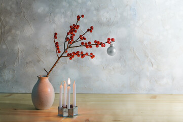 Minimalist first advent with four small candles, one is burning and a berry branch with a silver...