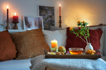Fototapeta na wymiar Relaxation with tea, candles and autumn decoration on a tablet in front of the couch in the cozy living room, copy space, selected focus