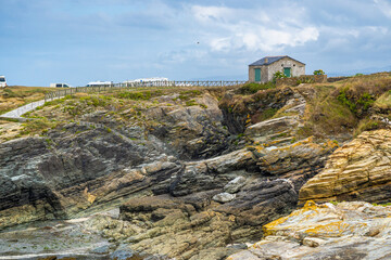 Beautiful rugged view of the coast of Galicia with the sea entering the rocks with moss and lichen and a rural road that leads to a rural house on the top of the hill with many motorhomes in the backg