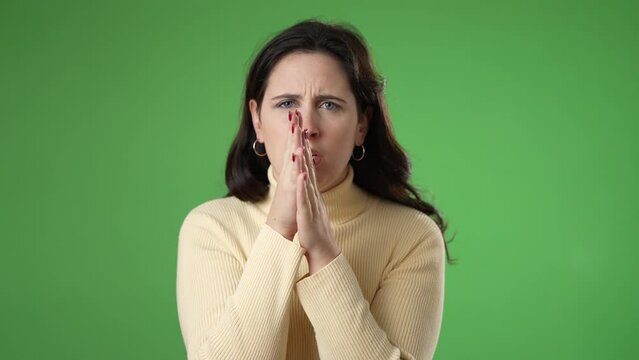 Young worried pleading woman 20s hold hands folded in prayer begging about something making wish keep fingers crossed isolated on green screen background studio. People lifestyle concept 