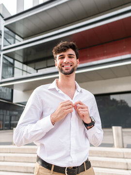 Cheerful young man in white shirt standing near modern building
