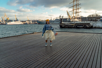 Outdoors fashion portrait of a beautiful middle aged woman walking on the beach. Marine background. Dressed in a stylish warm blue sweater, yellow skirt and beret.