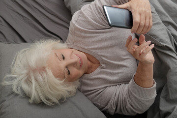 Happy elderly lady using smartphone in bed
