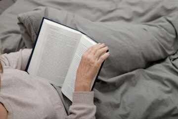 Anonymous senior woman reading book on bed