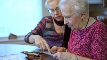 Elderly woman looks at photos with daughter. Senior woman sitting in the dining room looking at photographs with daughter. Brain training. Memory activity.
