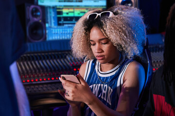 Woman using smartphone while sitting on armchair in recording studio