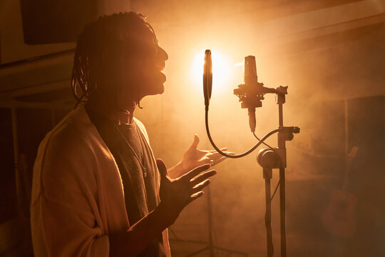 Black singer recording song in studio standing against glowing light