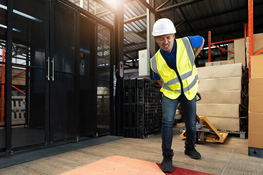Portrait, Tired millennial Asian male warehouse worker pulling a pallet truck, suffering from back pain, working in warehouse.