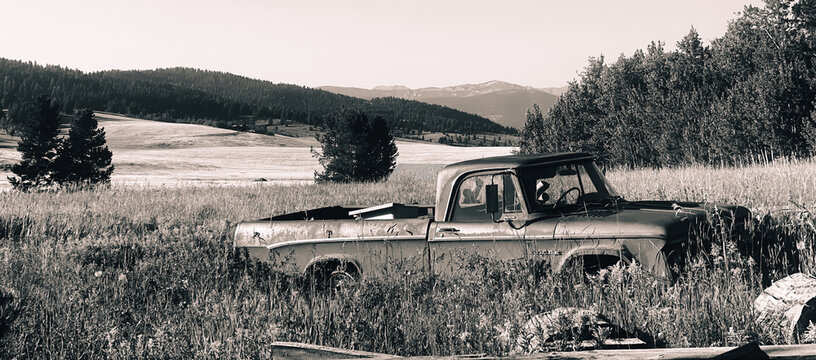 Old Red Vintage Truck in Green Grassy Meadow with Yellow flowers and Mountains in Background with Blue Sky