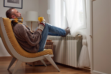 Man in sweater and hand gloves indoors on a chilly winter day, energy and gas crisis, cold room, heating problems. - obrazy, fototapety, plakaty