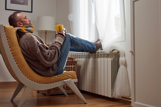 Man in sweater and hand gloves indoors on a chilly winter day, energy and gas crisis, cold room, heating problems.