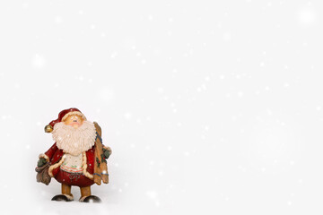 Santa Claus figurine holding christmas gifts and wooden ski on white snowy winter background