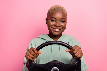 Photo of young pretty taxi driver female with short fair haircut holding steering wheel isolated on pink color background