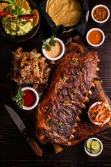 Vertical top view of grilled gourmet ribs on a wooden board surrounded by sauces