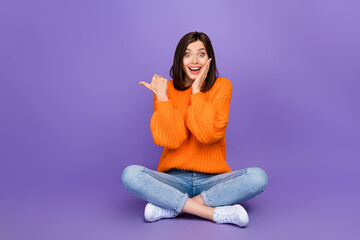 Full size photo of nice young girl impressed point copyspace sit floor wear trendy knitwear orange look isolated on violet color background