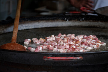 Pieces of speck bacon cubes being roasted and cooked on an outdoor stove at a Hungarian food festival
