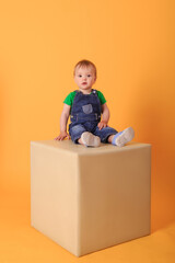 A little boy sitting on a light-colored pouf. Studio shot of a child against a yellow background