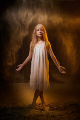 A girl in a white shirt and with long hair, looking like a ghost. A young model at a photo shoot with smoke, fog, flour, dust. A little fairy girl on a dark black background