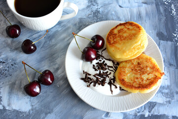 urkrainian syrniki on white plate with cherry, chocolate and yoghurt isolated, close-up