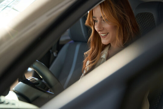 Joyful female is seated in driver seat of car