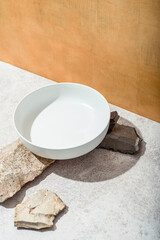White dish on stones, corner composition. Cookware trends - simple shapes, stones, solid reds, Earth tones, eco friendly design, set design