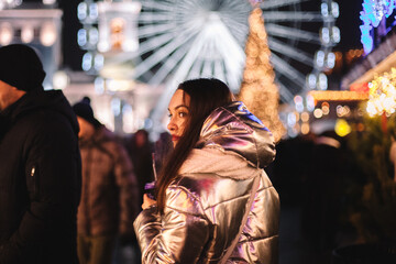 Young woman looking back while walking in Christmas market in city at night