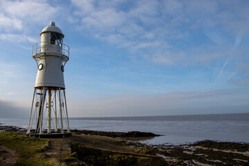 Lighthouse tower by the sea with coast and clouds