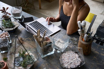 Young woman working on laptop from her stylish plant studio
