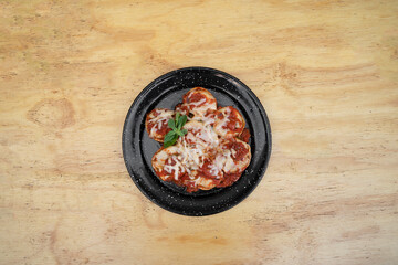Stuffed pasta. Top view of sorrentinos with a mediterranean tomato sauce and provolone cheese in a black dish on the wooden table. 