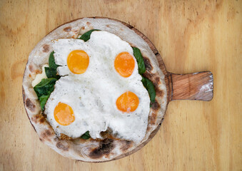 Top view of a pizza with mozzarella cheese, spinach and fried eggs, on the wooden table. 