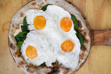 Top view of a pizza with mozzarella cheese, spinach and fried eggs, on the wooden table.