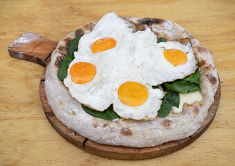Closeup view of a pizza with mozzarella cheese, spinach and fried eggs, on the wooden table.