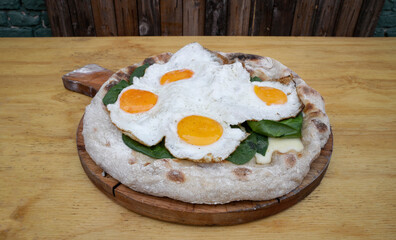 Closeup view of a pizza with mozzarella cheese, spinach and fried eggs, on the wooden table. 