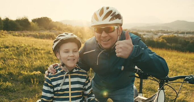 Father teaching son to ride bicycle. Happy cute boy in helmet learn to riding a bike in park on green meadow in summer day at sunset time. Family weekend. 4K video Slow motion
