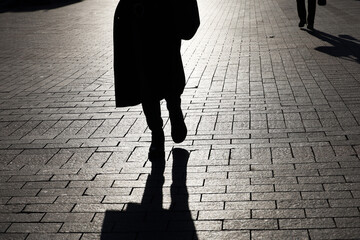 Black silhouette and shadow of lonely woman walking on a street and person on background. Female...