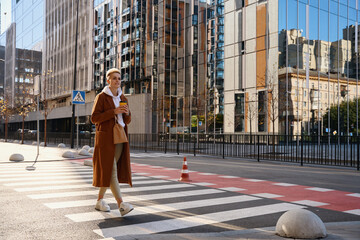 Stylish woman in a wool coat walks along a crosswalk