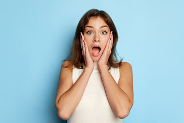 Portrait of young beautiful woman posing with shocked expression isolated over blue studio background. Unexpected news